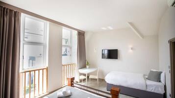 A hotel room with a bed, a desk, a chair, a TV, and a balcony.