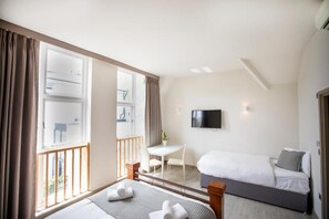 Habitación de hotel con cama, escritorio, silla, televisor y balcón.