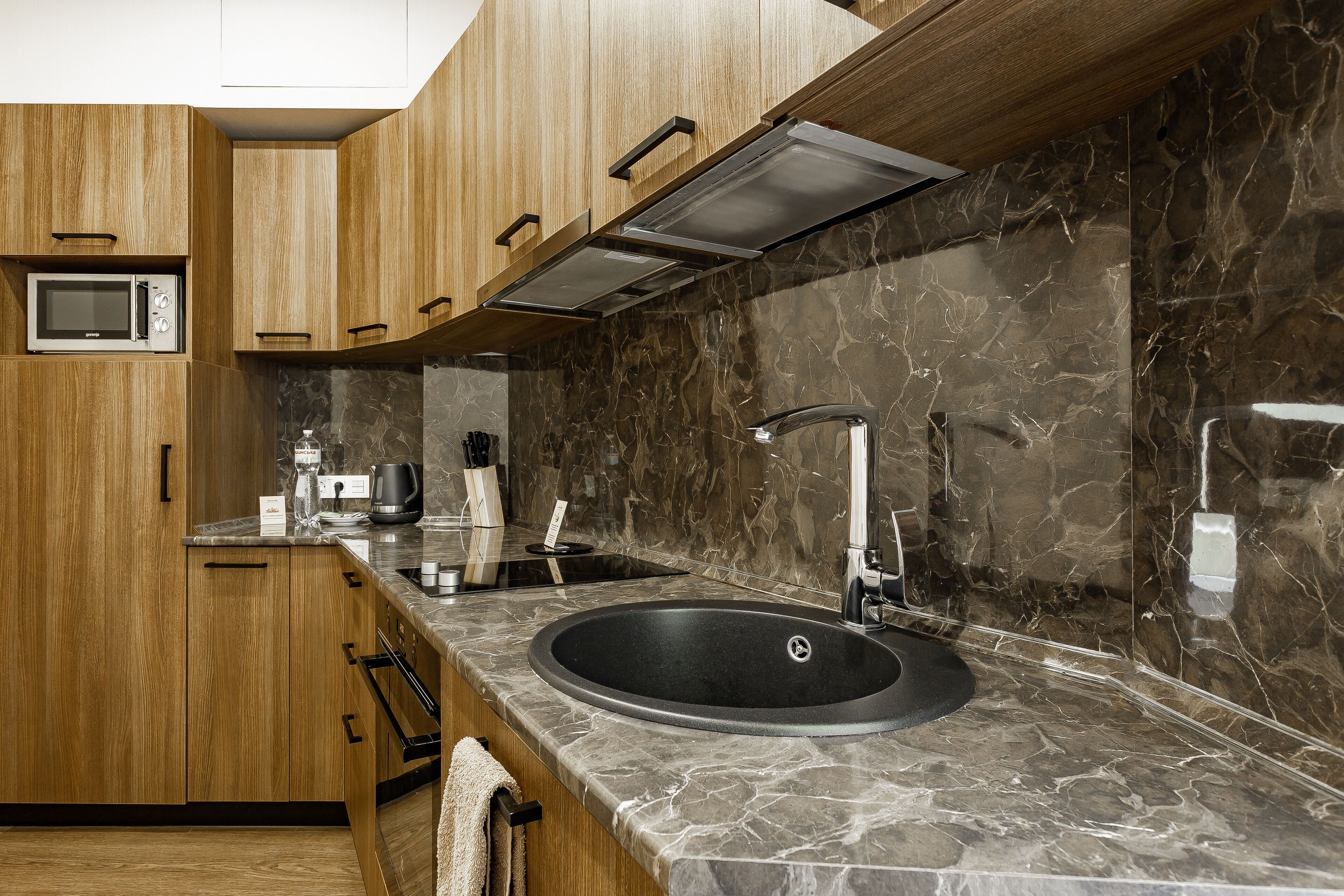 Una cocina moderna con armarios de madera, un lavamanos negro y un salpicadero de mármol.
