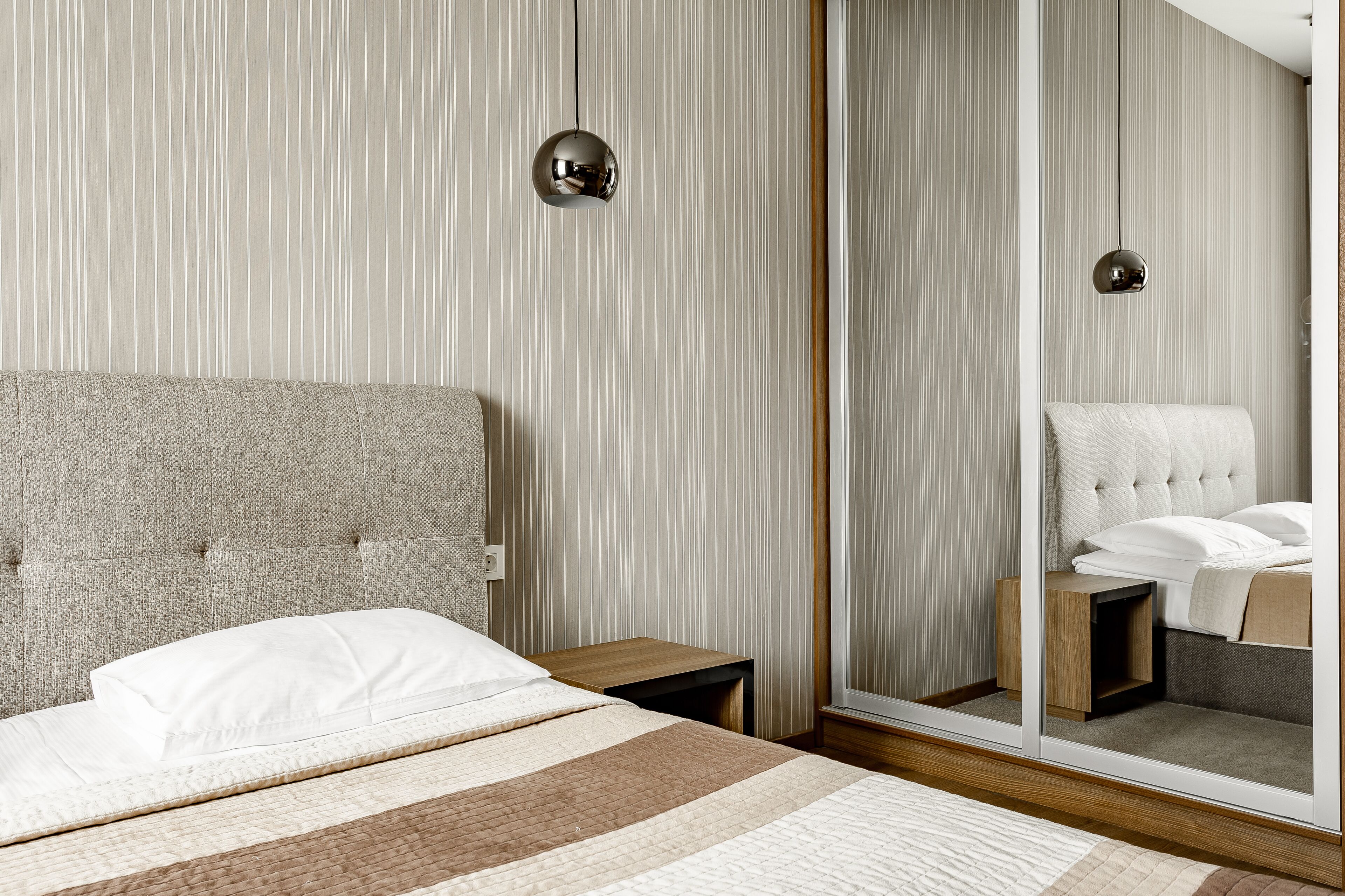 A modern bedroom with a large bed, a nightstand, a mirror, and a hanging light fixture.