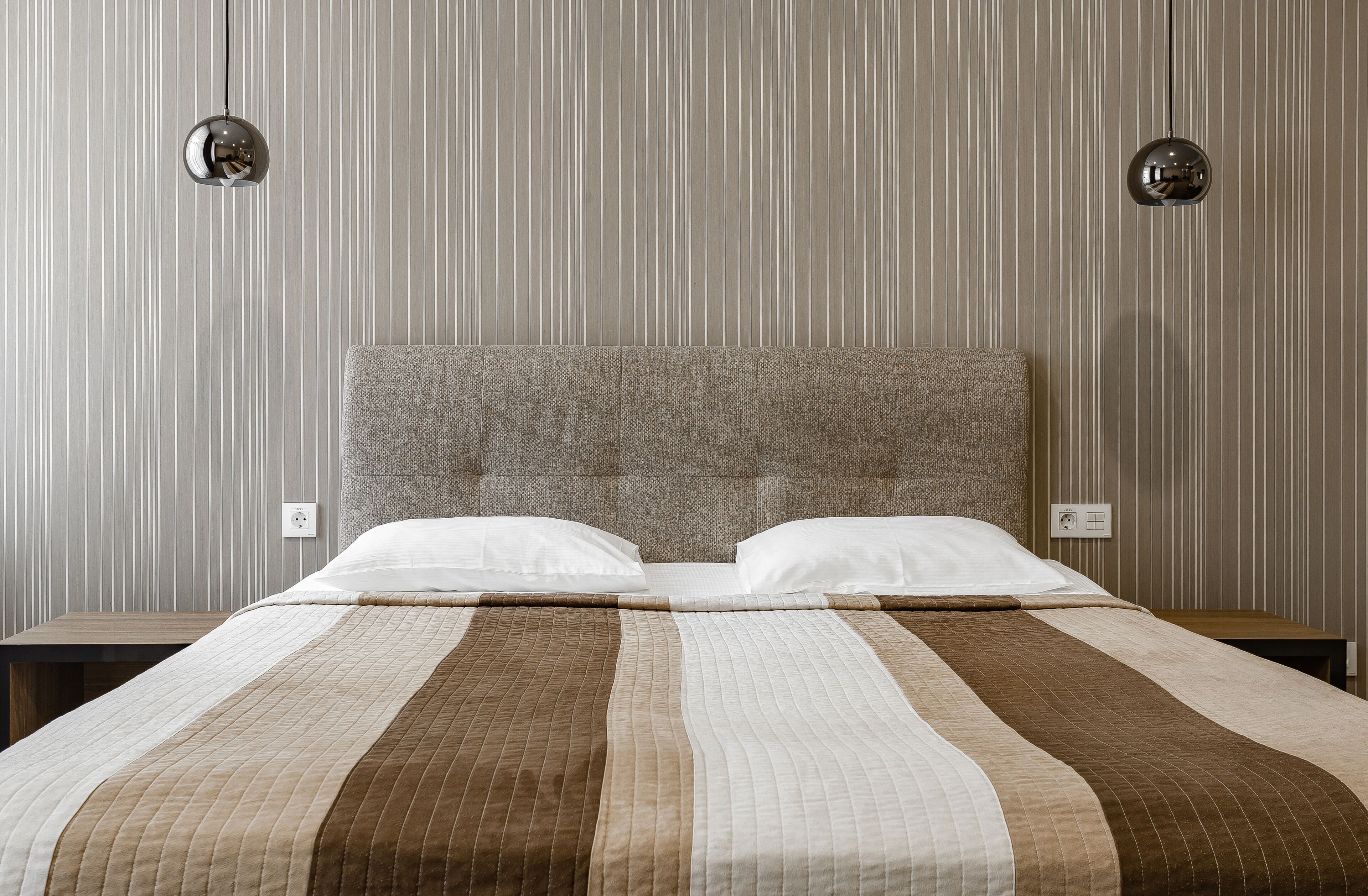 Un letto rifatto con cura, una coperta a righe, due comodini e una testiera.