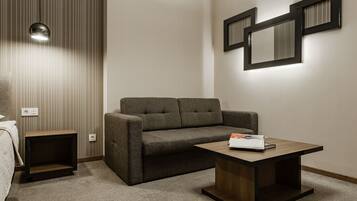 A modern hotel room with a brown sofa, a wooden coffee table, a small side table, and a wall-mounted mirror.