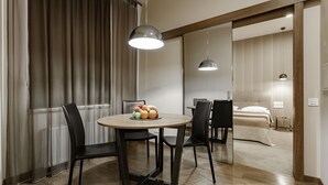 A modern hotel room with a dining area featuring a round table, chairs, and a fruit bowl. The room has a wooden floor, a bed with a white headboard, and a large window with curtains. - Senator Maidan (Kyiv)