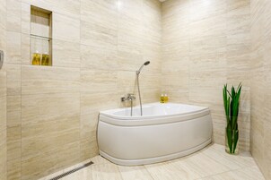 Un baño moderno con una bañera independiente, un estante de vidrio con artículos de aseo y una planta verde alta.