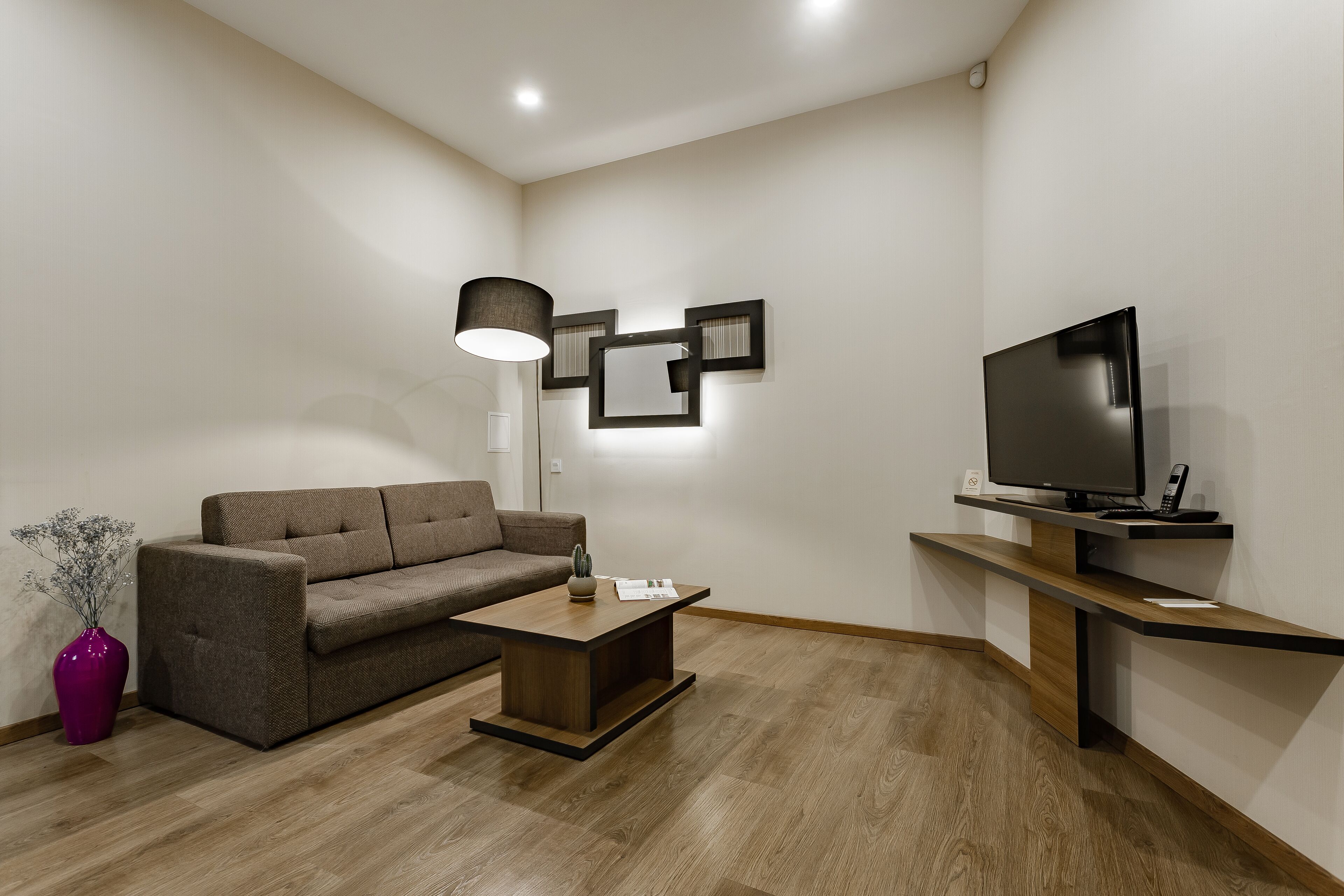 Una sala de estar moderna con sofá, mesa de centro, televisor y lámpara.