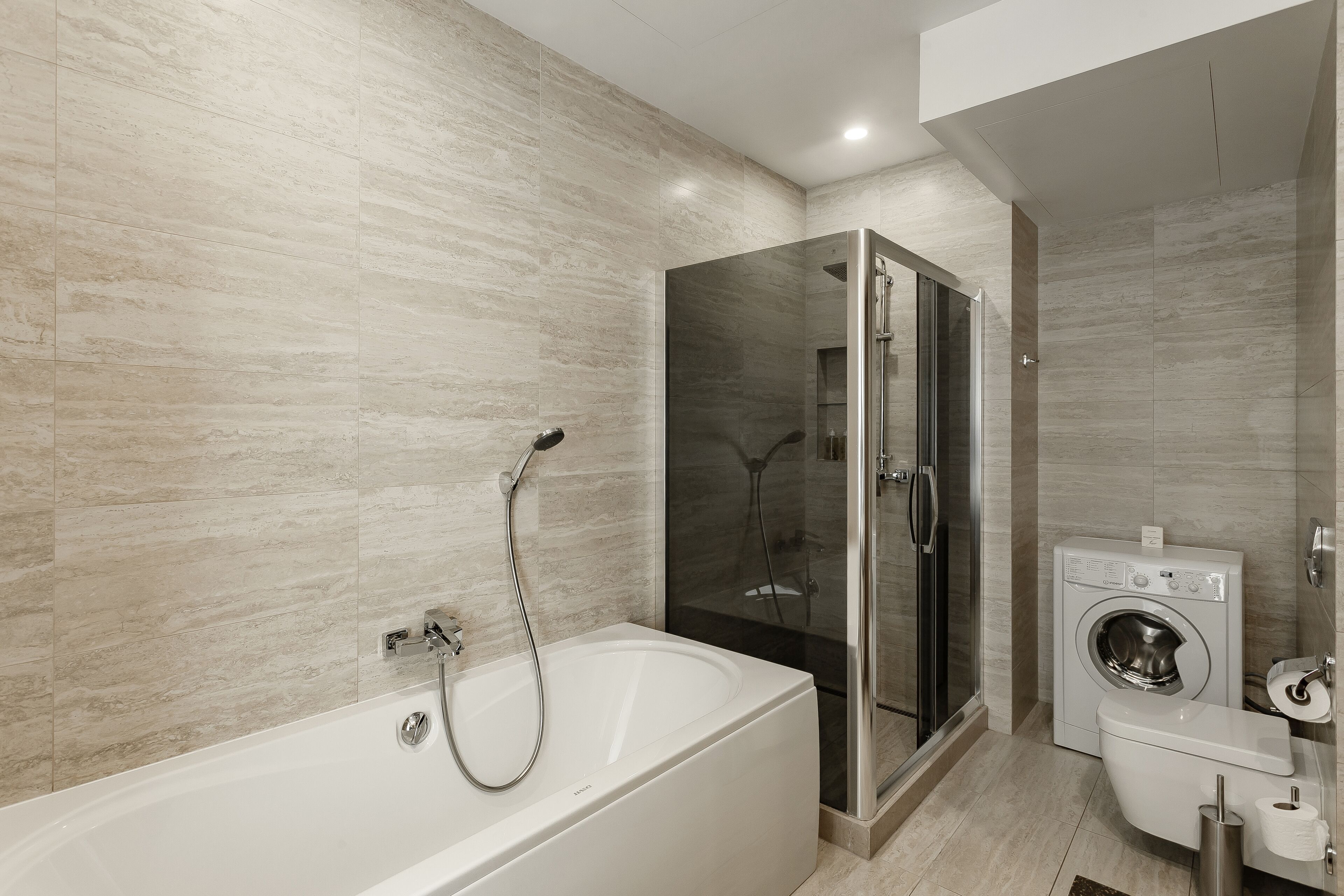 Un baño moderno con bañera, cabina de ducha de vidrio y lavadora integrada.