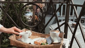 A wicker tray with two cups of coffee, a pastry, and a newspaper on a balcony railing. - Senator Maidan (Kyiv)
