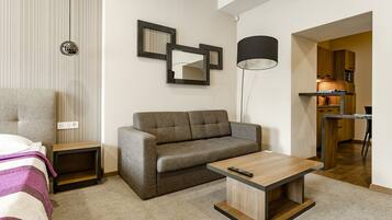 A modern hotel room with a sofa, a small table, a bedside table, and a lamp.