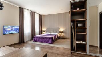 A modern hotel room with a large bed, a television mounted on the wall, a wardrobe, and a bedside table.