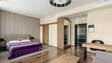 A modern hotel room with a large bed, a wooden desk, and a wardrobe.