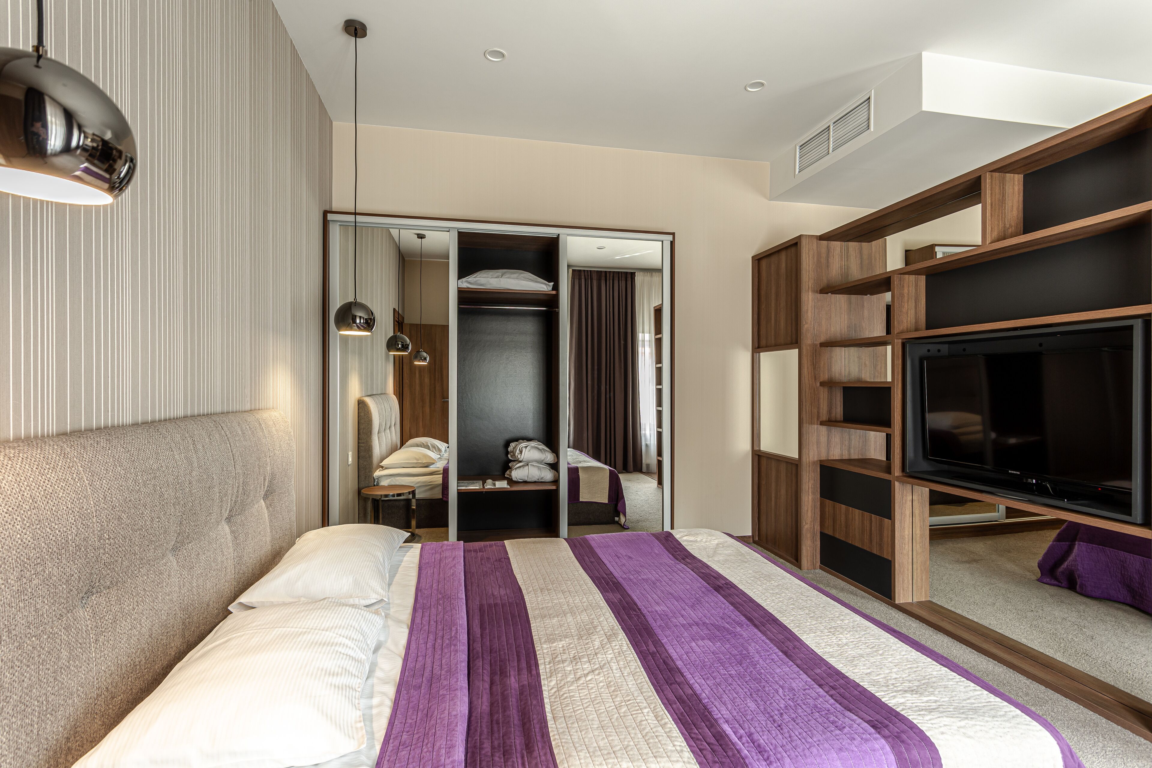 Una habitación de hotel moderna con una cama grande, televisión, armario y espejo.