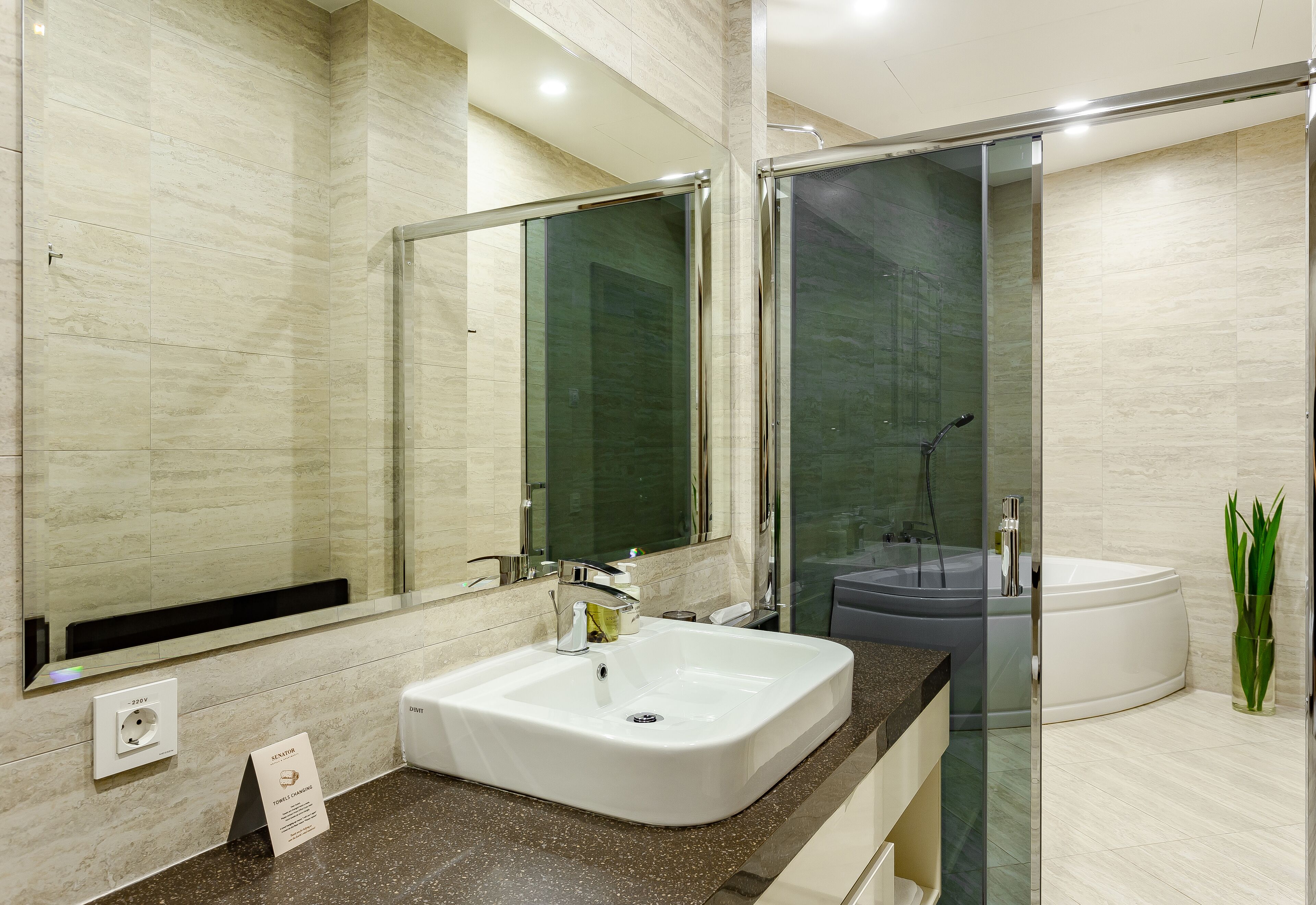 A modern bathroom with a large mirror, a white sink, a glass-enclosed shower, and a bathtub.