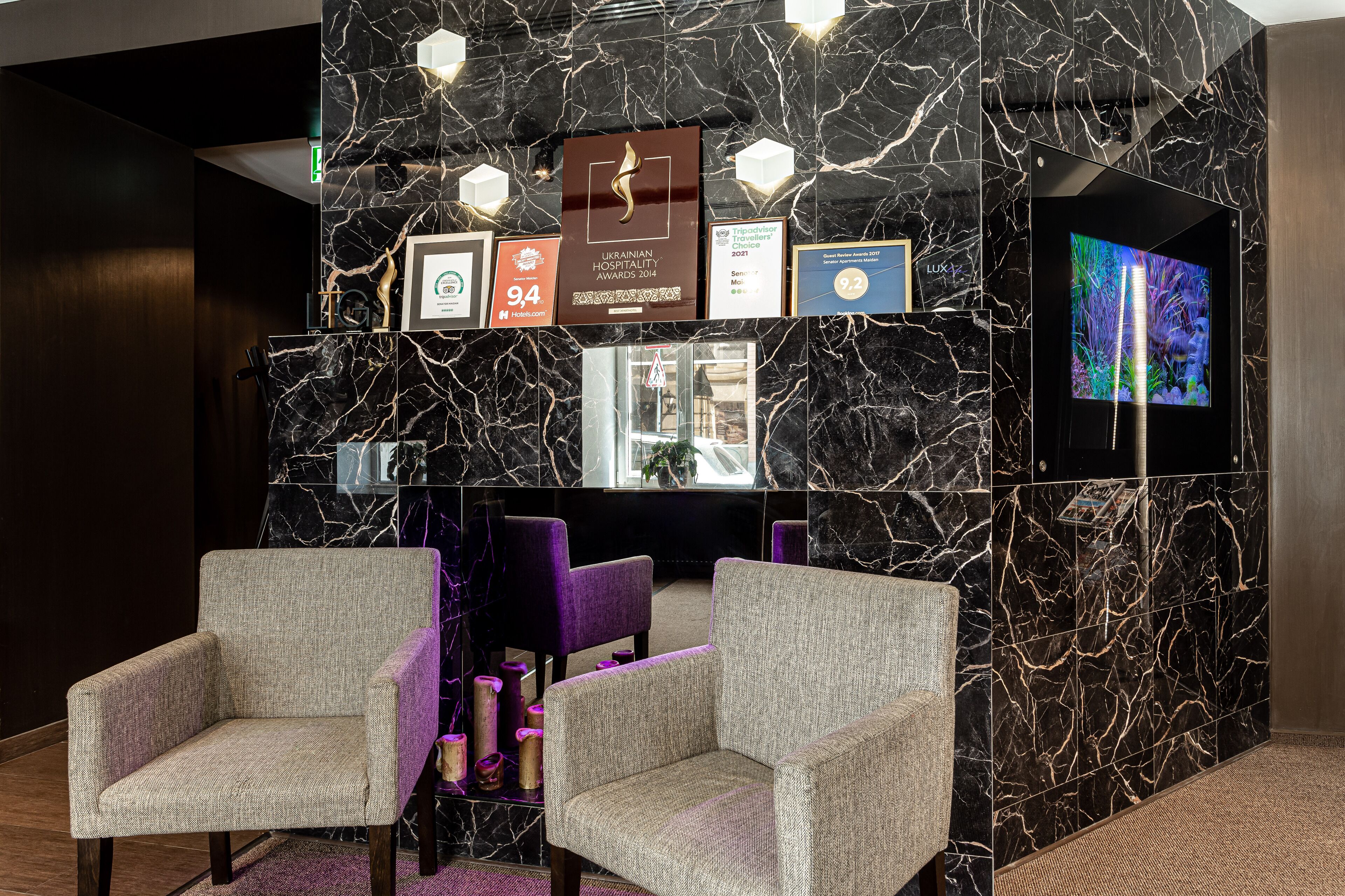 A lobby with marble walls, framed awards, a television, and seating.