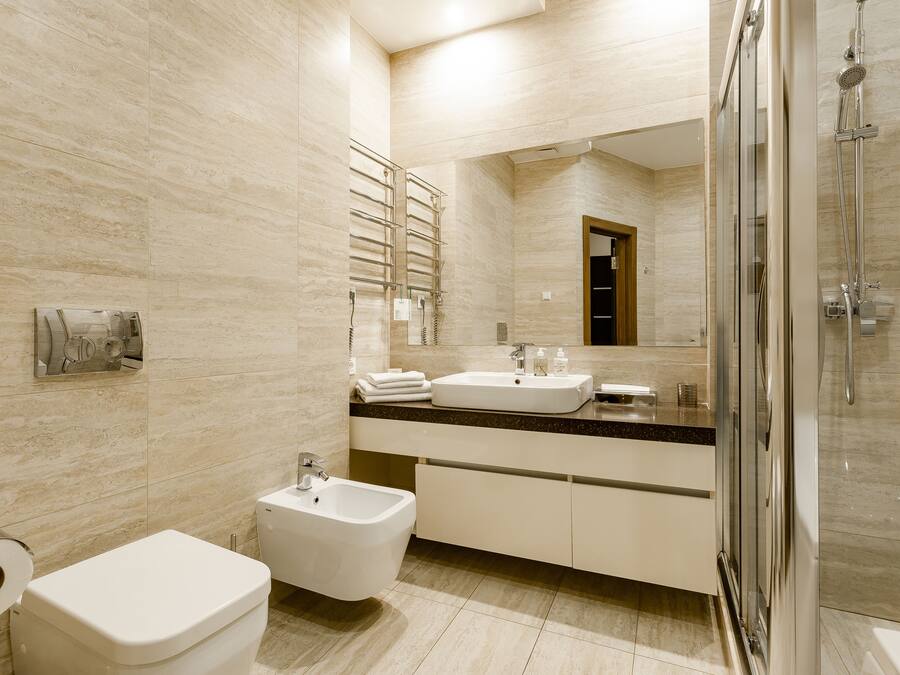 Un baño moderno con bidé, inodoro, dos lavabos, un espejo grande y cabina de ducha con paredes de vidrio.