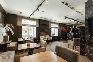 Un moderno vestíbulo de hotel con zonas de estar, una recepción y un amplio ventanal que proporciona luz natural.