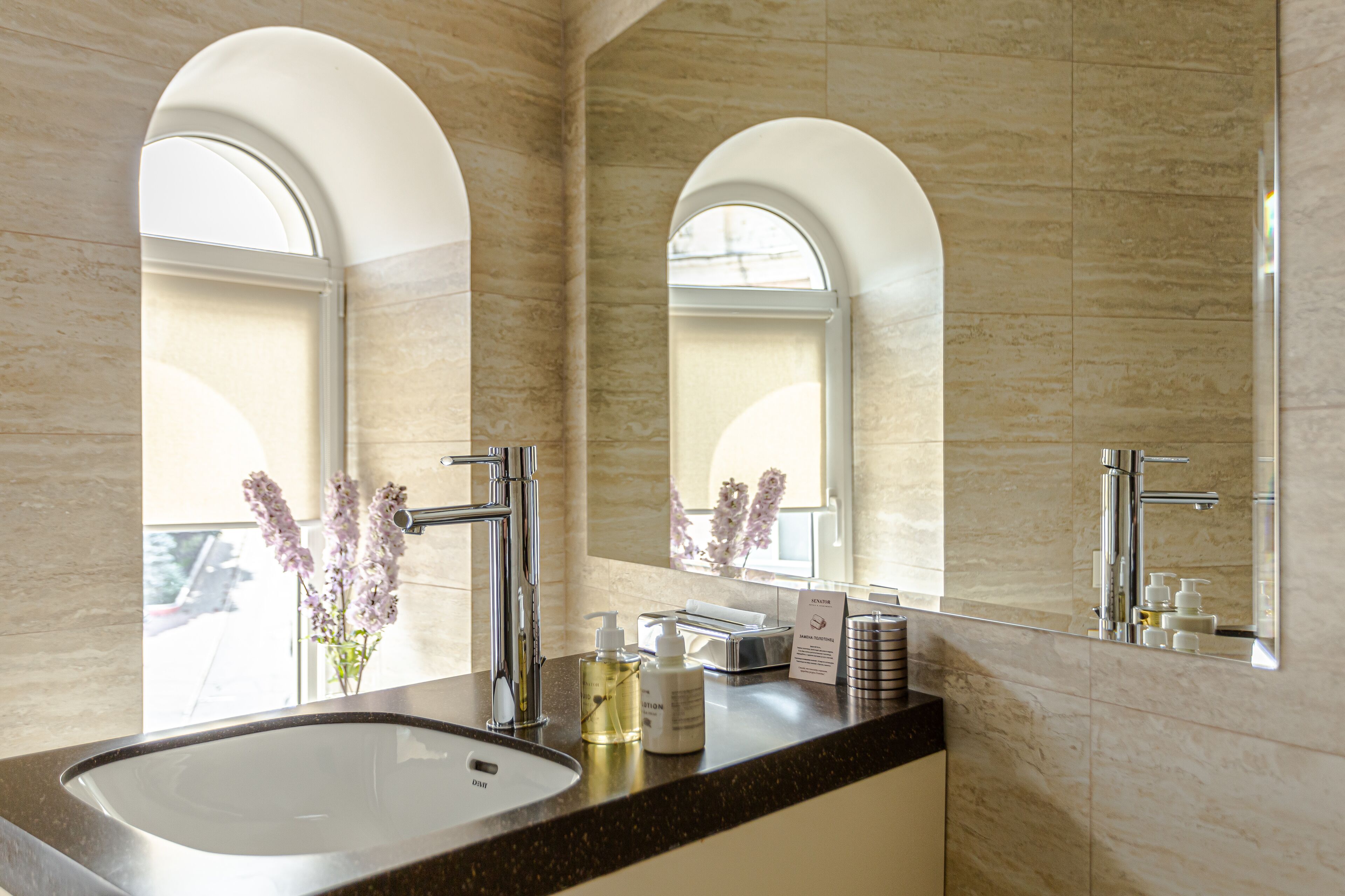 Un baño con un lavamanos grande, dos grifos, un espejo y una ventana de arco.