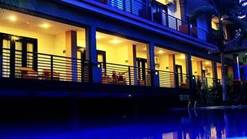 Um hotel com vários andares, varandas, piscina e iluminação acolhedora.