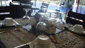 A dining table set with white dishes and silverware, surrounded by chairs, in a room with a view of palm trees and a pool. - Taman Tirta Ayu (Tuban)
