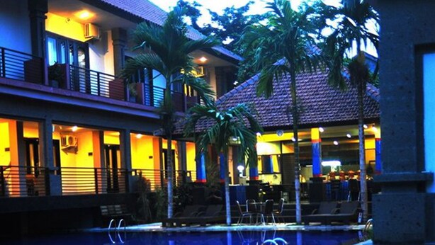 A swimming pool with a tiled deck, surrounded by buildings with balconies and palm trees. - Taman Tirta Ayu (Tuban)