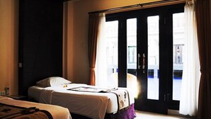 A hotel room with two beds, a large window with curtains, and a view of the street outside. - Taman Tirta Ayu (Tuban)