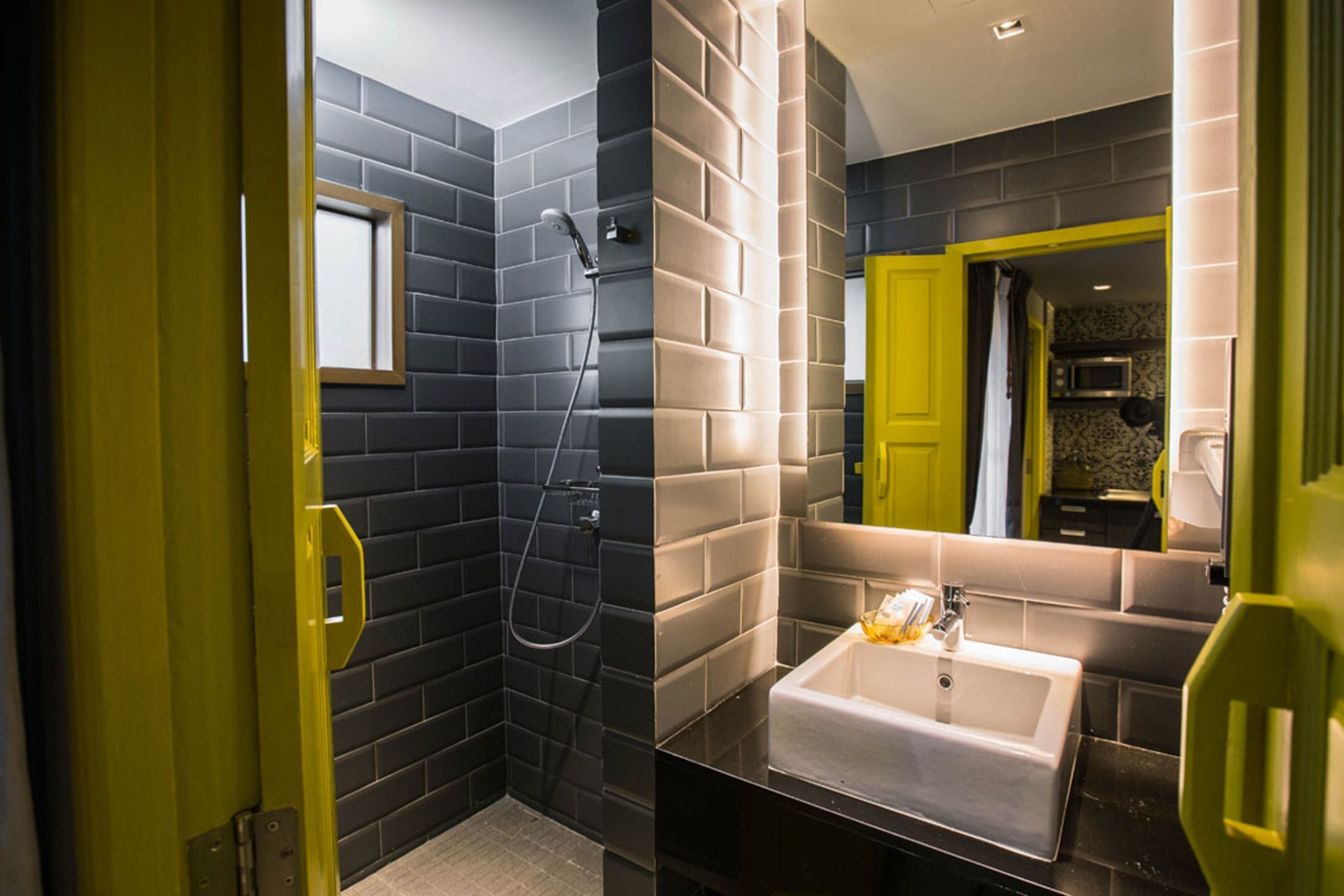 A modern bathroom with dark tiled walls, a white sink, and a shower area.