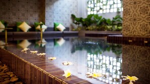 Un espace piscine intérieur paisible, avec un sol carrelé, un coin salon doté de coussins et de plantes en pot.