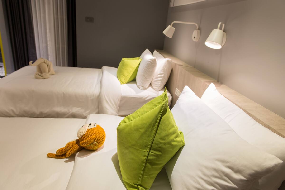 A hotel room with two beds, each with white bedding and green pillows. There are two bedside lamps and a telephone on the left bed.