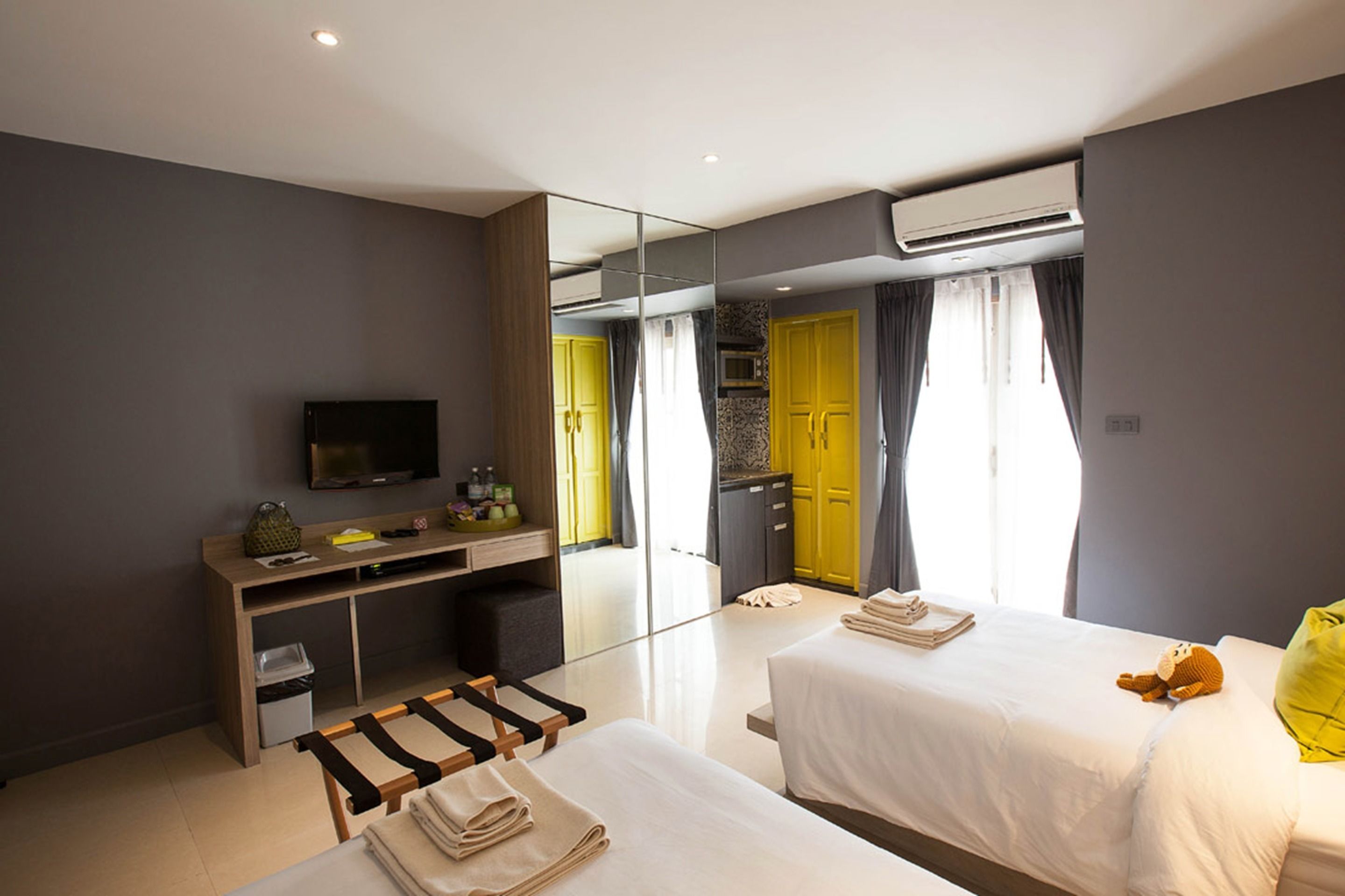 Una habitación de hotel moderna con dos camas, un escritorio, un televisor y un espejo grande.