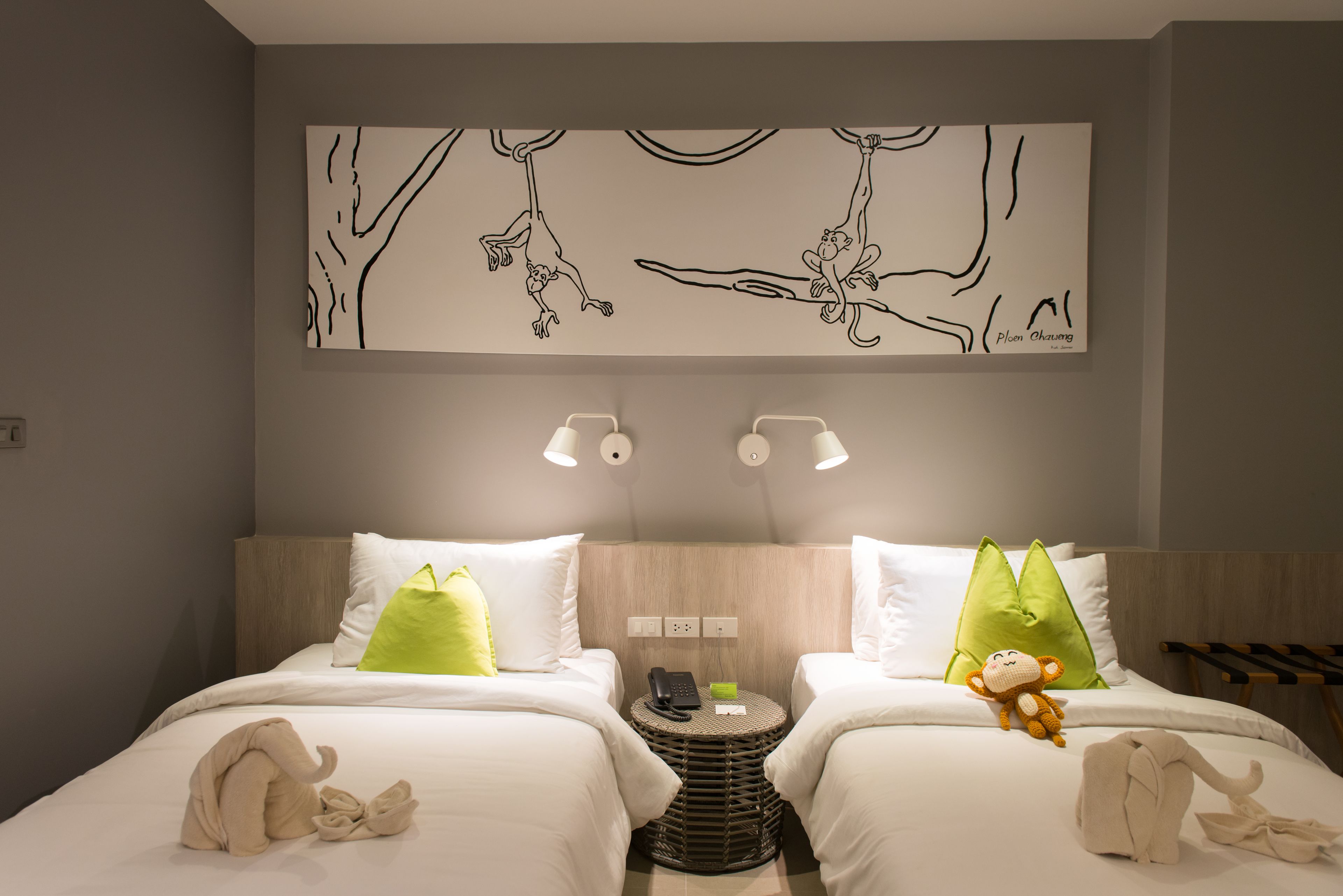 A hotel room with two beds, a wall art of monkeys, a small round table with a phone and a bowl, and a towel on the floor.