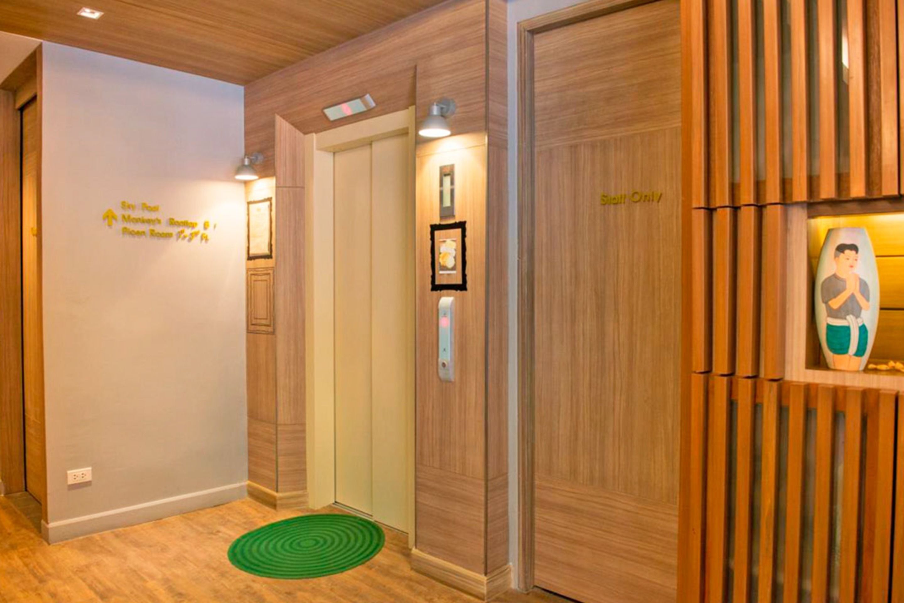 A hotel lobby with wooden paneling, a green mat on the floor, and a sign indicating the direction to the room service and elevator.