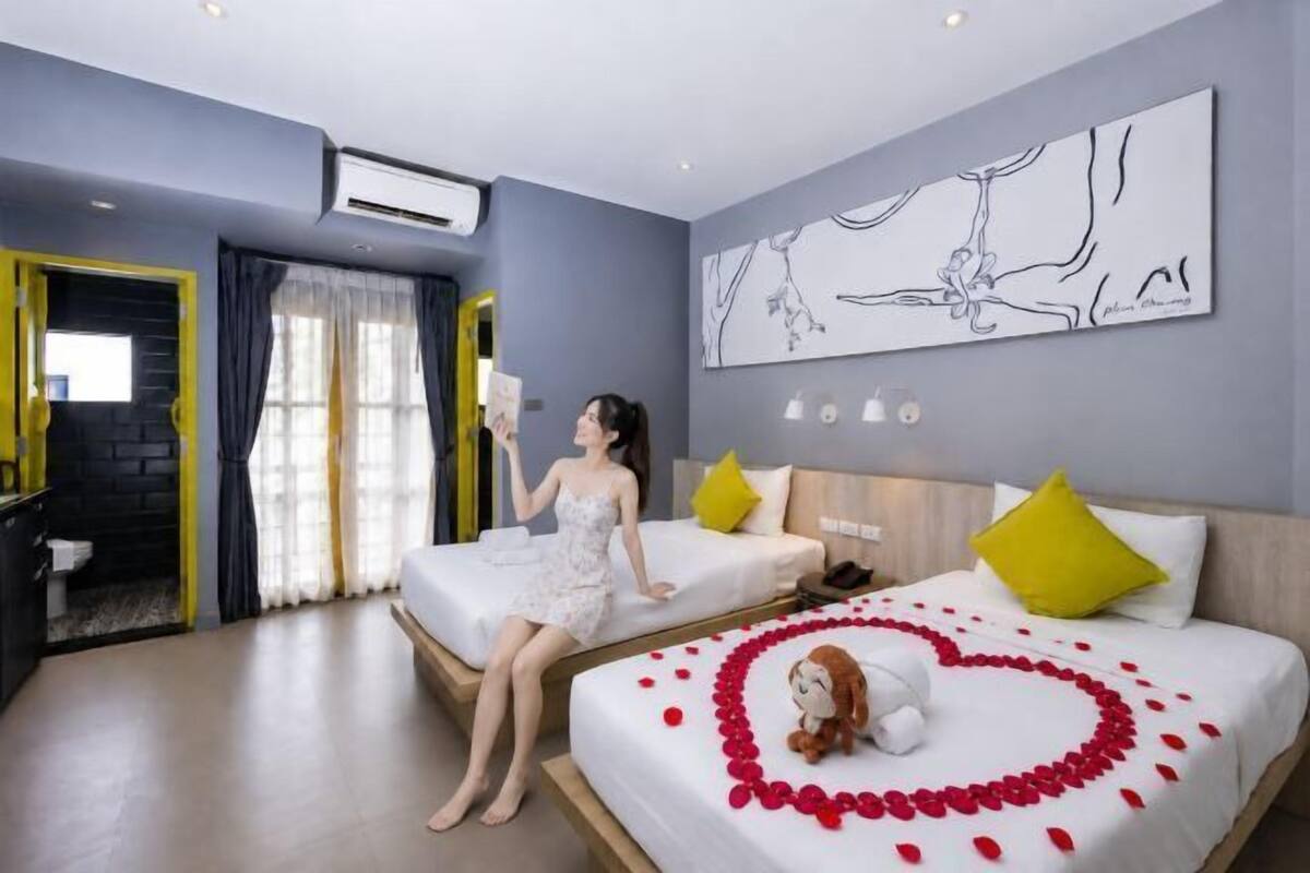 A hotel room with two beds, a large window with curtains, a wall-mounted air conditioner, and a piece of abstract art.
