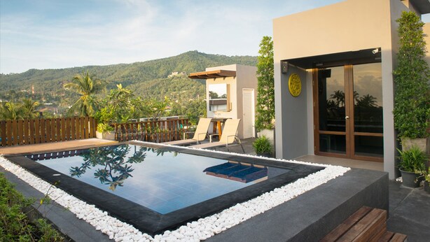 Une piscine moderne offrant une vue dégagée sur le paysage environnant, une terrasse en bois et un bâtiment doté d’une entrée en verre.