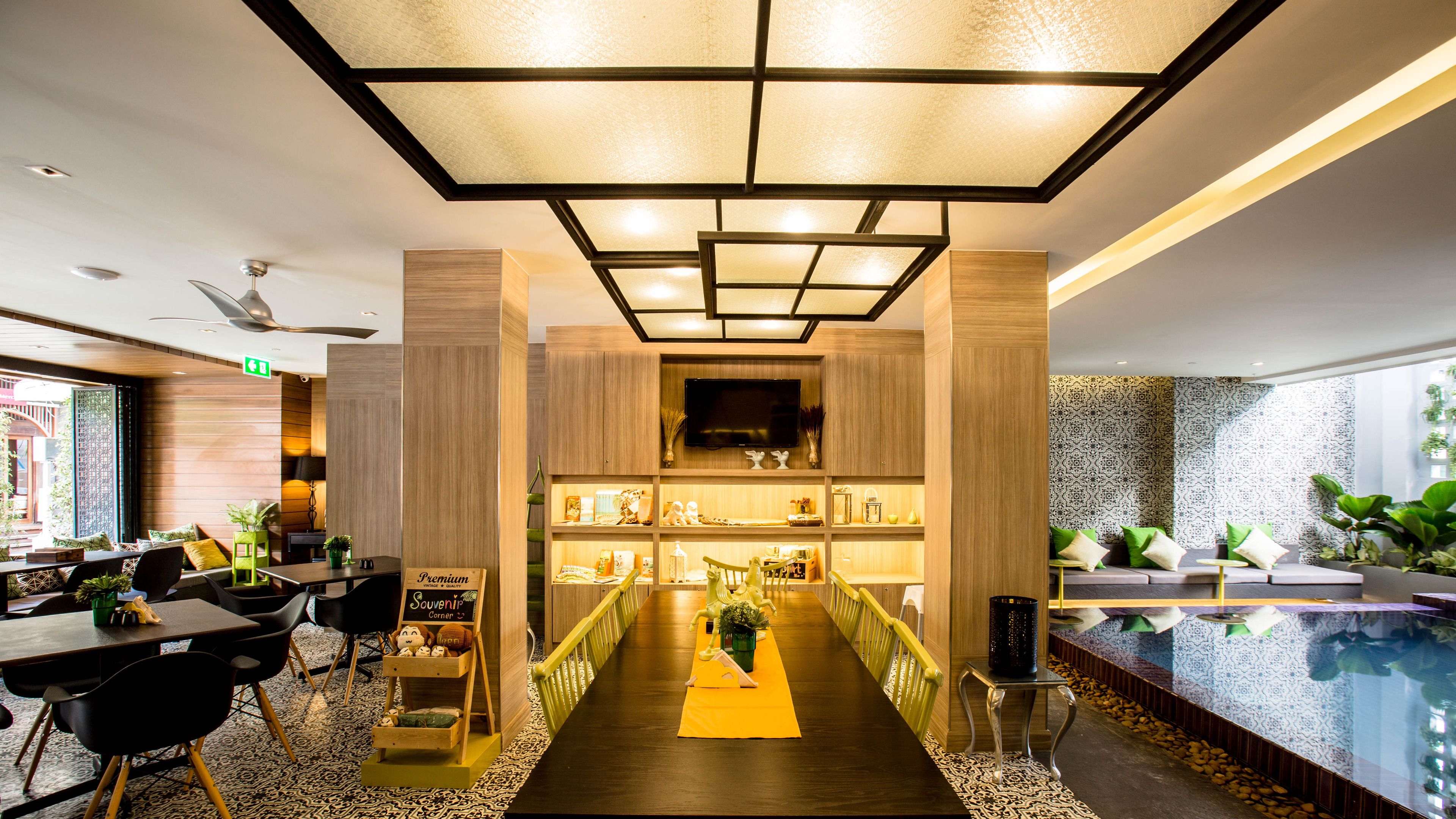 A modern hotel lobby with a central reception desk, a seating area with chairs, a pool area, and a decorative plant display.
