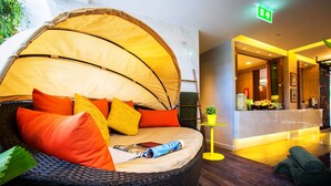 Une pièce chaleureuse avec un lit en osier, des touches de jaune vif et une petite table agrémentée d’une plante.