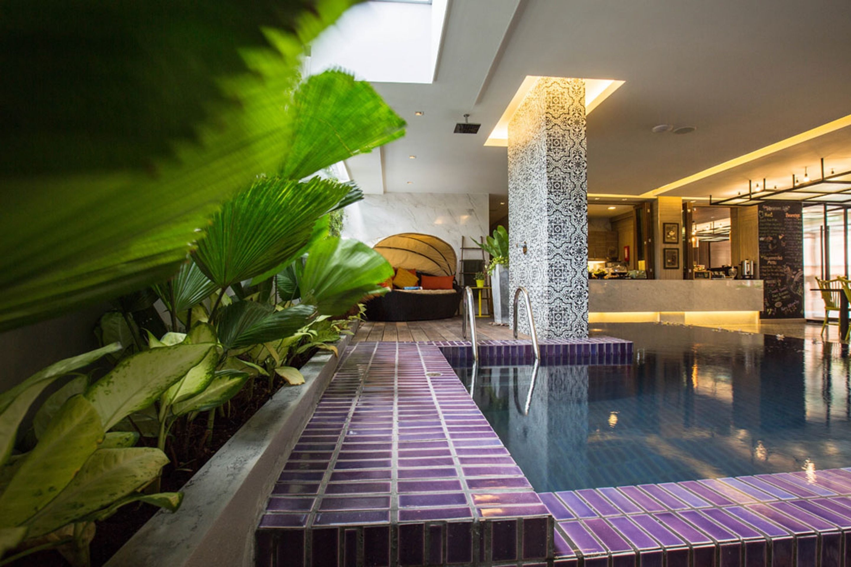 A modern indoor pool area with a tiled floor, a central column, and surrounding greenery.