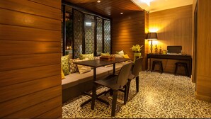 A modern interior with a wooden panel wall, a dining area with a table and chairs, a sofa with cushions, a small desk with a lamp, and a patterned rug. - Ploen Chaweng Koh Samui by Tolani (Koh Samui)