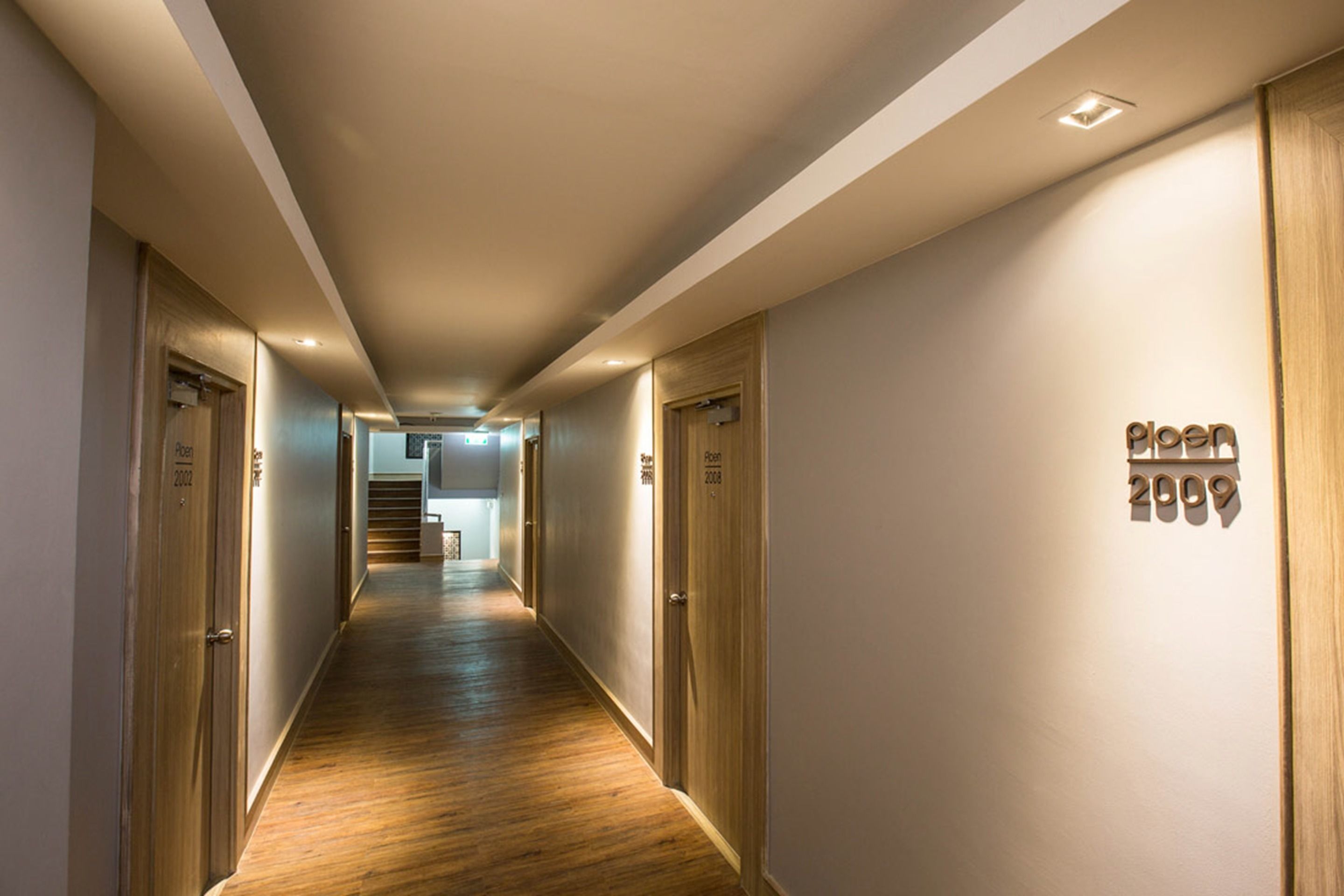 A hallway with wooden flooring, doors on both sides, and a sign on the right wall.