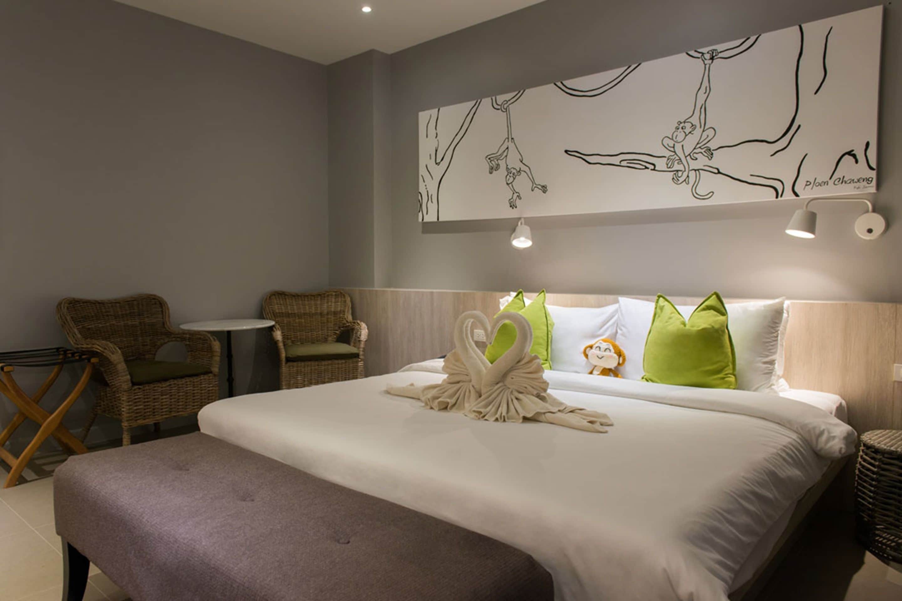 Ein Hotelzimmer mit einem Bett, einer Bank, zwei Korbstühlen, einem kleinen Tisch und einem Wandbild.
