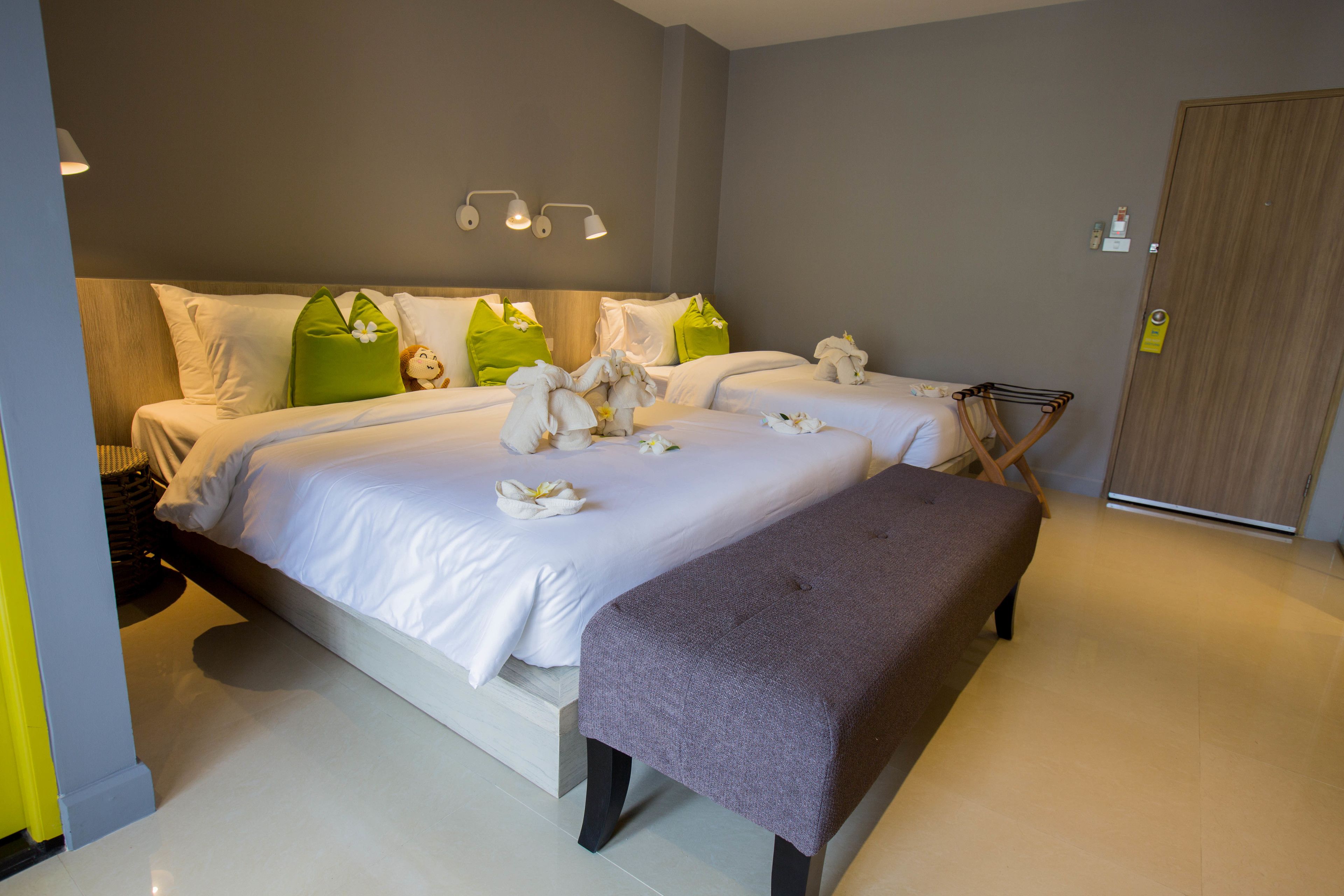A modern hotel room with two beds, a bench, and a wooden wardrobe.
