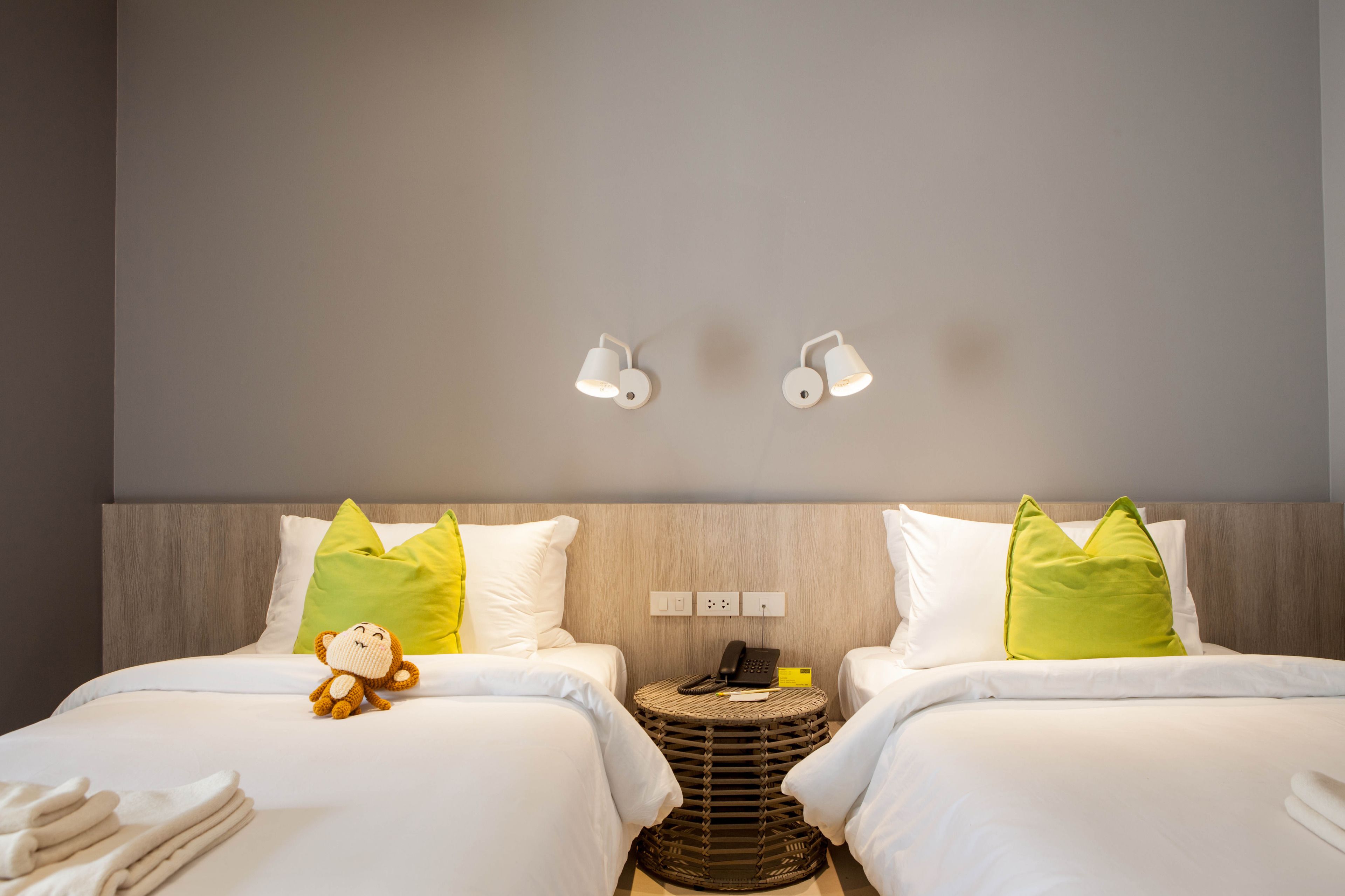 A hotel room with two beds, a small round table, a teddy bear, and a wall-mounted phone.