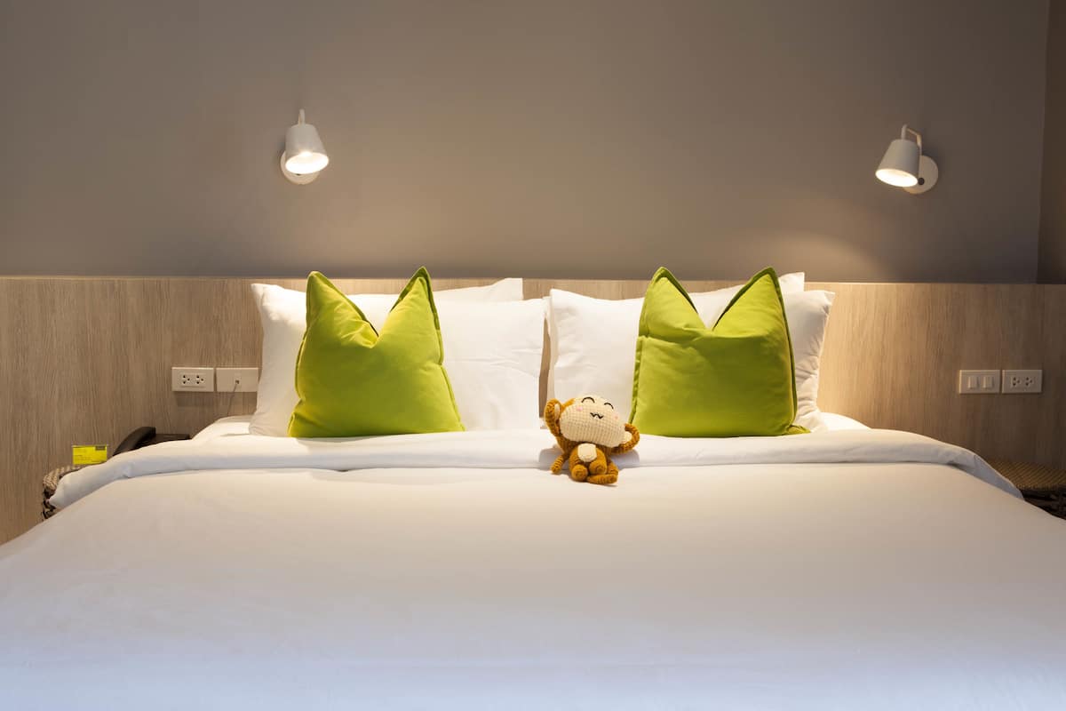 A neatly made bed with white bedding and two green pillows, a plush toy in the center, and two wall-mounted light fixtures.