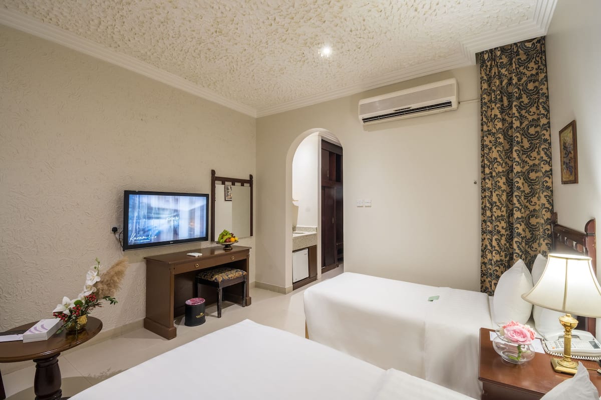 A hotel room with two beds, a television, a desk with a mirror, and an air conditioning unit.