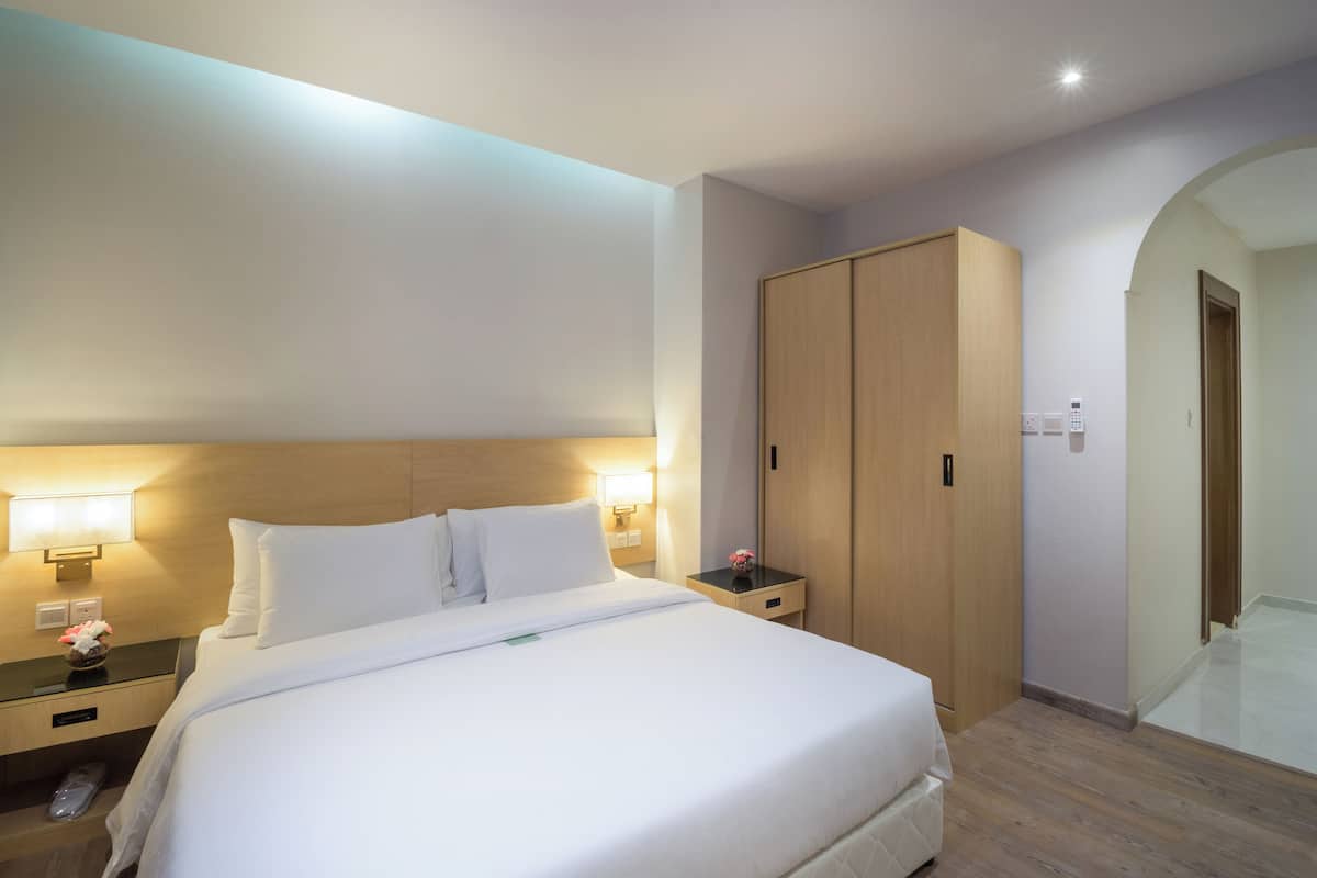 A hotel room with a large bed, bedside lamps, a wooden wardrobe, and a small table with a vase of flowers.