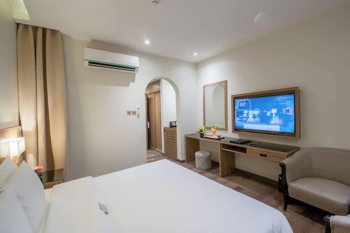 A hotel room with a bed, a desk with a computer, a chair, a television, and an air conditioning unit.