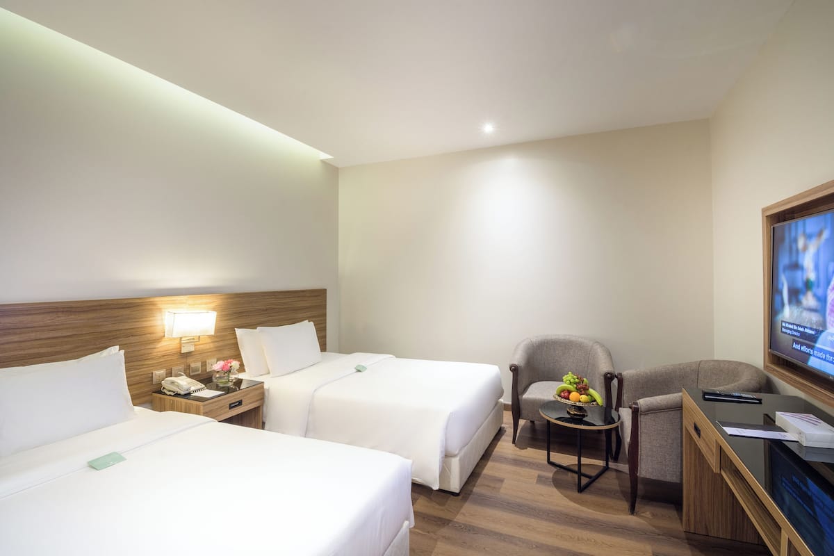 A hotel room with two beds, a desk with a television, a chair, and a small table with fruit.