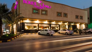 A hotel with a prominent neon sign, multiple windows, and a parking area with several cars. - Boudl Al Masif (Riyadh)