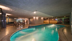 An indoor swimming pool with a tiled edge, a seating area with chairs, and a television screen mounted on the wall. - Boudl Al Masif (Riyadh)