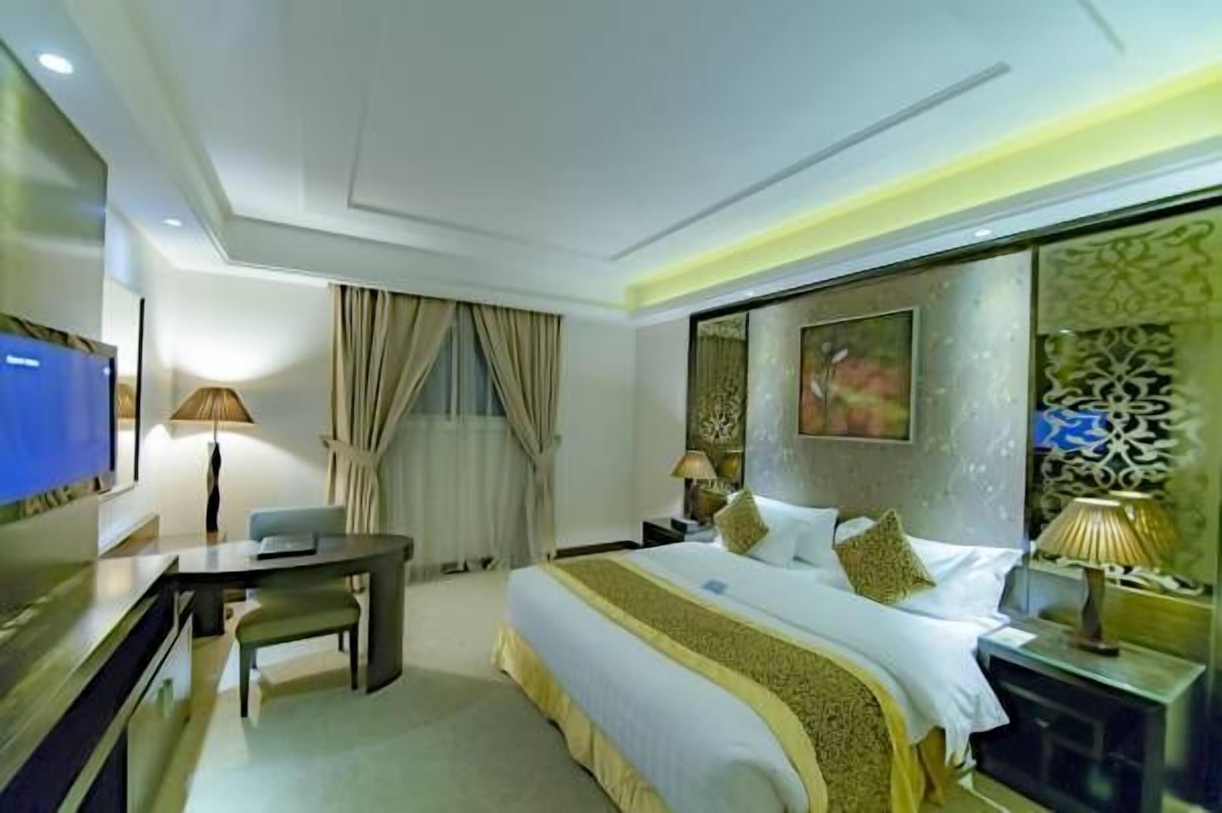Quarto de hotel com cama, escrivaninha, televisão e um detalhe decorativo na parede.