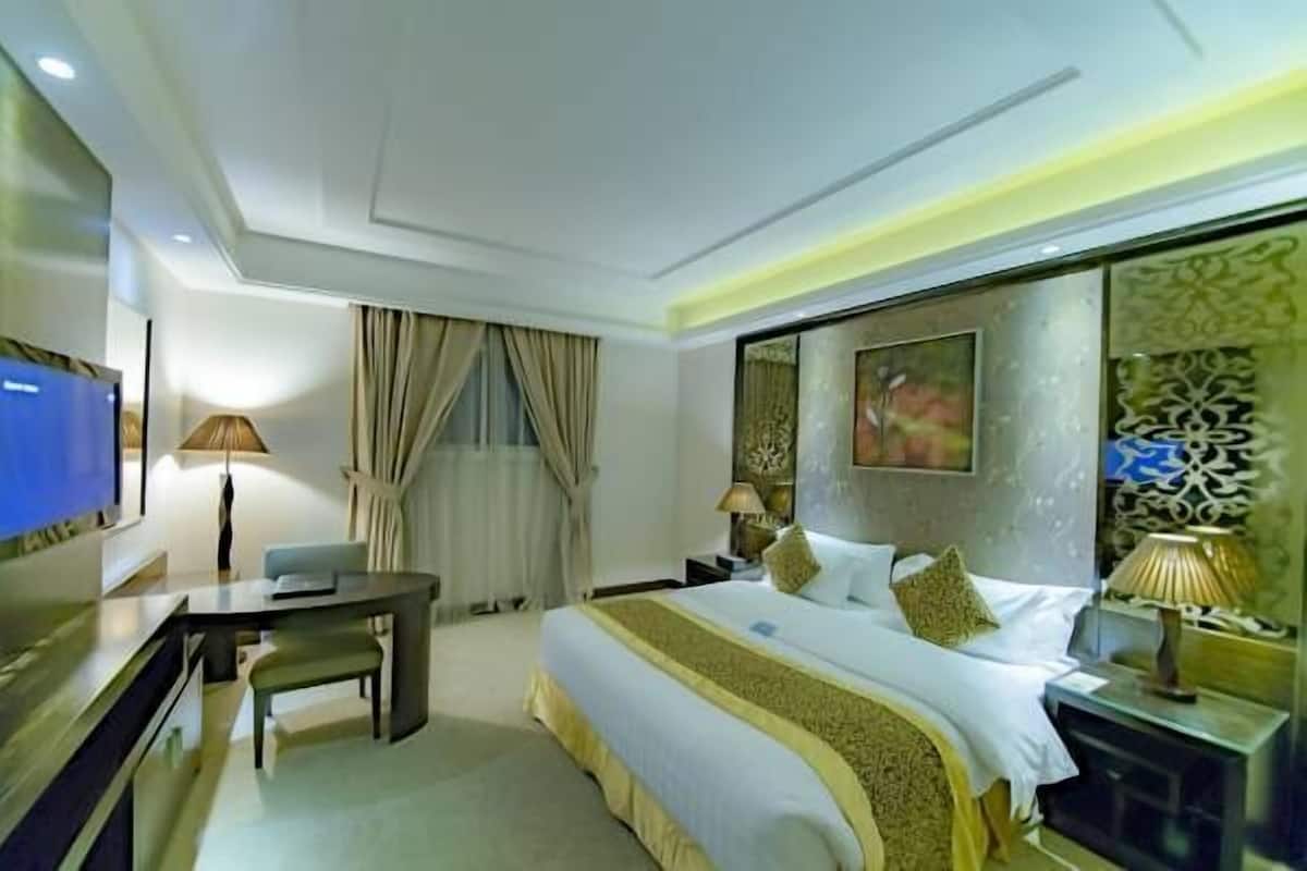 Quarto de hotel com cama, escrivaninha, televisão e um detalhe decorativo na parede.