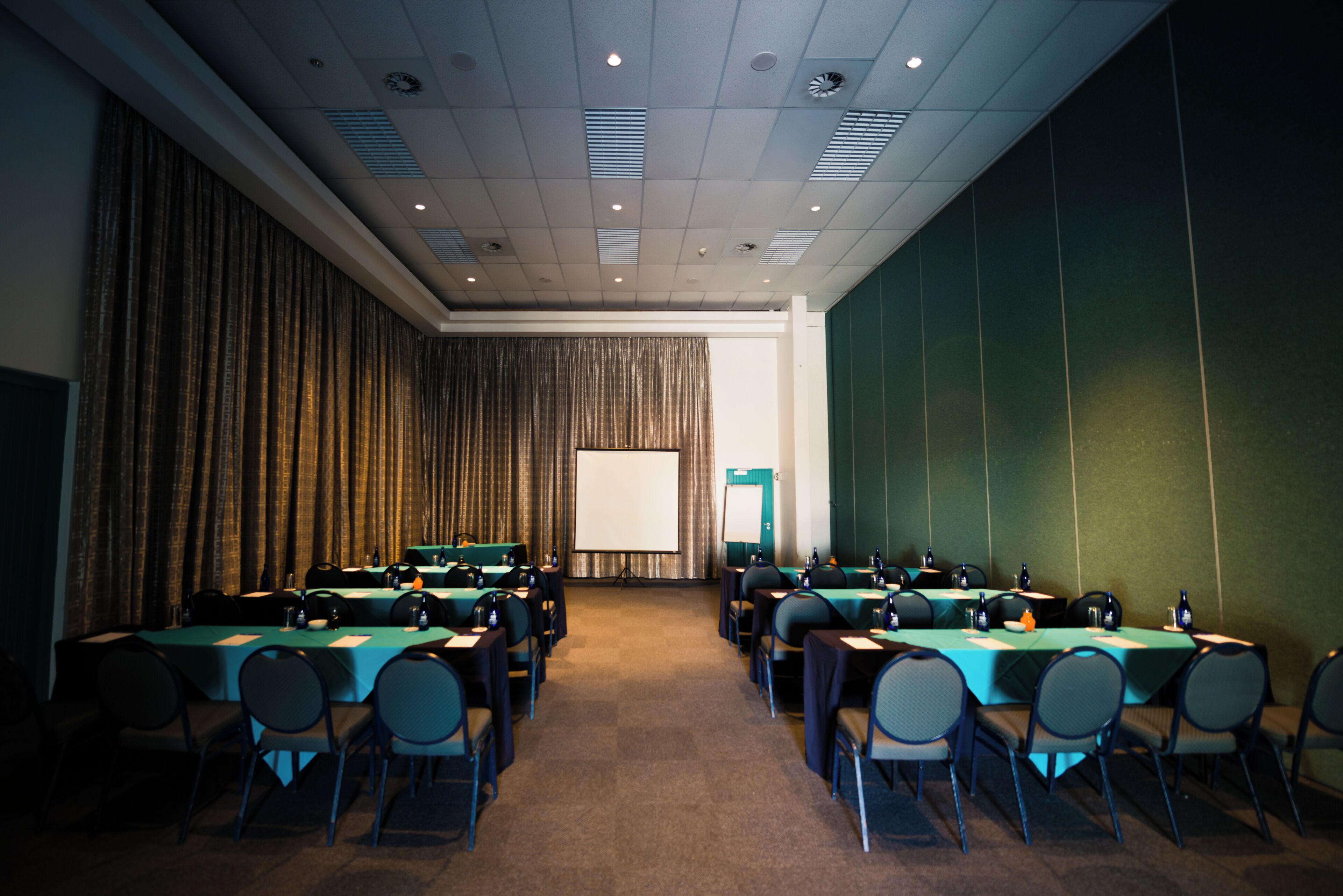 A conference room with multiple tables and chairs, a projector screen, and a green wall.
